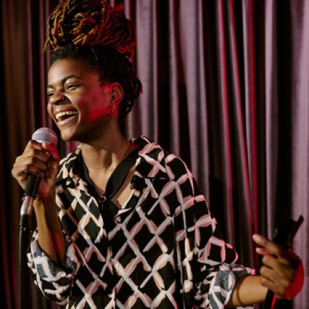 Smiling performer holding microphone while performing on stage. Vibrant energy and joy radiating from the performance as the crowd engages with the act